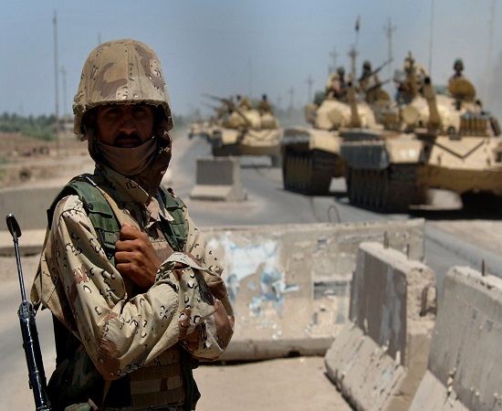 An Iraqi Army soldier stands guard duty while Iraqi T 72 tanks pass through a highway checkpoint in Mushahada, Iraq - عملیات ارتش و نیروهای مردمی عراق در منطقه البوذیاب